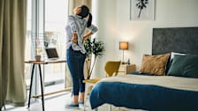 A woman holding her back while standing at her desk.