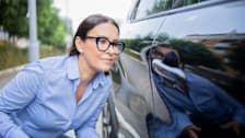 A woman shopping for a car and inspecting a scratch on the door.
