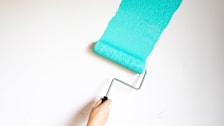 detail of hand using paint roller with blue paint on white wall