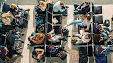 overhead view of rows of seats at airport gate with people waiting with luggage