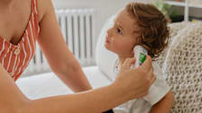 adult person checking temperature of toddler using an in-ear thermometer