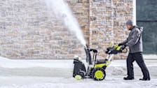 A man pushing a Ryobi RY40870 Snow Blower through snow on a driveway