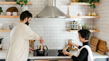 couple using cooktop with range hood and open shelving