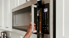 A person opening a microwave in a kitchen