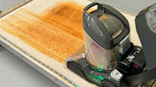 a Consumer Reports tester using the Hoover ONEPWR Smartwash Cordless Carpet Cleaner to clean a stained carpet sample.