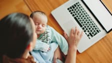 a mother holding an infant while working on a laptop