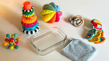 An assortment of baby toys on a table with soapy water and a cleaning cloth
