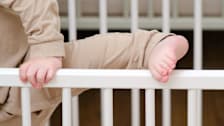 close up of a toddler attempting to climb over a crib railing