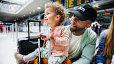Toddler sits in their dads lap at the airport.