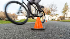 low angle view of person riding electric bike on asphalt path, going between orange traffic cones with house and grass in background