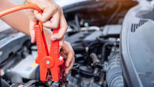 a person jump-starting a dead car battery with a jumper cable