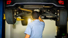 back of mechanic looking at undercarriage of raised car in repair shop