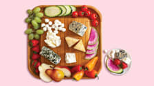 Cheese board with blue, Parmesan, mozzarella, feta, goat cheeses and various fruits and vegetables.