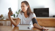 person sitting at table in living room checking blood pressure with smartphone in other hand