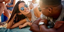 Two people with different skin tones talking on a beach with friends.
