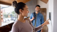 Couple leaving their house and setting the alarm using a home automated system.