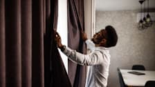 a man opening up blackout curtains in a dining room