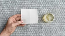 hand holding laundry detergent sheet next to liquid laundry detergent in cup