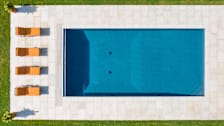 overhead view of pool with stone patio, 4 orange lounge chairs, and grass along outer edge