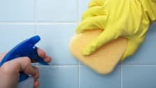 Closeup of hands cleaning shower tile.