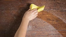 hand using yellow microfiber cloth to wipe off dust from wooden surface