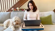 Woman using Arlo lap desk while sitting on couch with dog at her side.