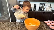 a young boy pouring cupcake batter into a mixing bowl
