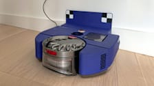 Dyson 360 Vis Nav Robot Vacuum docked against white wall and wooden floor