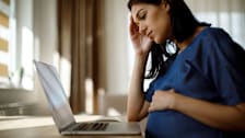 Pregnant woman with a worried face looking at a laptop.
