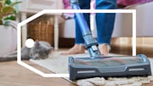 Woman using vacuum in home while cat lounges.