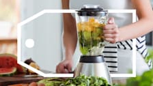 Woman using blender for smoothie with vegetables and fruits.
