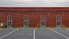 Empty parking spacing in front of brick building with dotted lines showing 4 EV chargers.