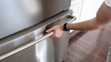 A person with their hand on the door of a stainless steel refrigerator.