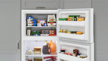 A top-freezer with its fridge and freezer doors open to show food inside, gray cabinets surround the fridge