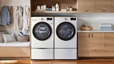 LG WM4000HWA washing machine and LG DLHC4002W dryer in laundry room with wood floor and cabinets, clothes hanging to the left of machines