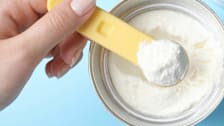 Hand seen from above scooping infant formula out of a container.