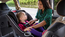 A mother buckling her toddler into a rear-facing car seat.