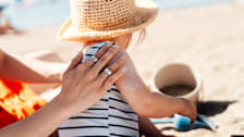 A person applying sunscreen to a baby on the beach.