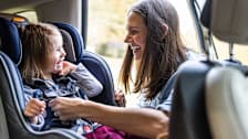 A caretaker tightening the straps on a toddler's car seat.