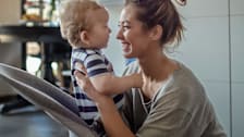 A smiling caregiver lifting a baby out of a baby bouncer.