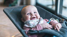 A smiling baby looking up in a baby bouncer.