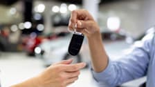 close up of hand holding car FOB, handing to another person's hand with blurred cars in background