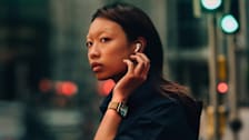 person wearing Apple Watch Series 10 on left wrist, hand up near ear that's wearing Apple AirPod