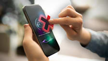 A person's finger is poised over an illustrated red X that is overlaid on the screen of a smart phone which is displaying an interactive AI bot.