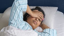close up of person laying in bed with hand over eyes and forehead as though they're tired and in pain