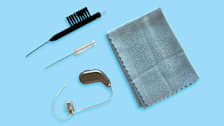 hearing aid, two different types of cleaning brushes, and microfiber cloth on blue background