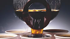 carafe filled with coffee being poured into paper cup with other paper coffee cups in background