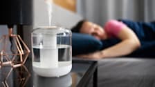 white humidifier on nightstand with lamp and person sleeping blurred in background