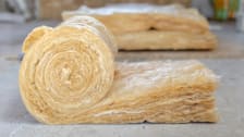 side view of roll of home insulation starting to unroll with more insulation blurred in the background