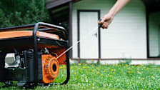 Arm pulling start cord of a generator, outside on the grass with home in background